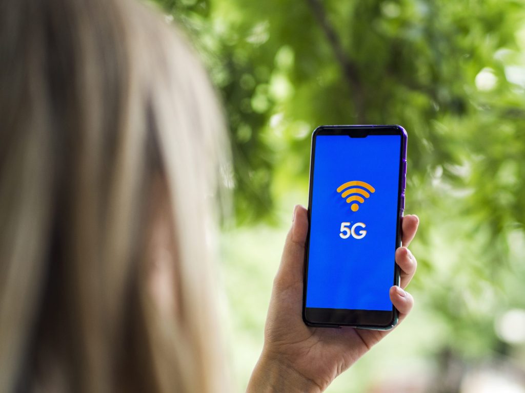 Main tenant un téléphone affichant le logo 5G sur fond naturel