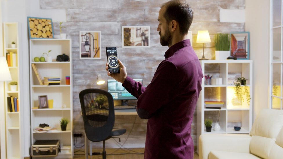 Homme pilotant sa maison connectée depuis son smartphone dans un intérieur moderne en Tunisie