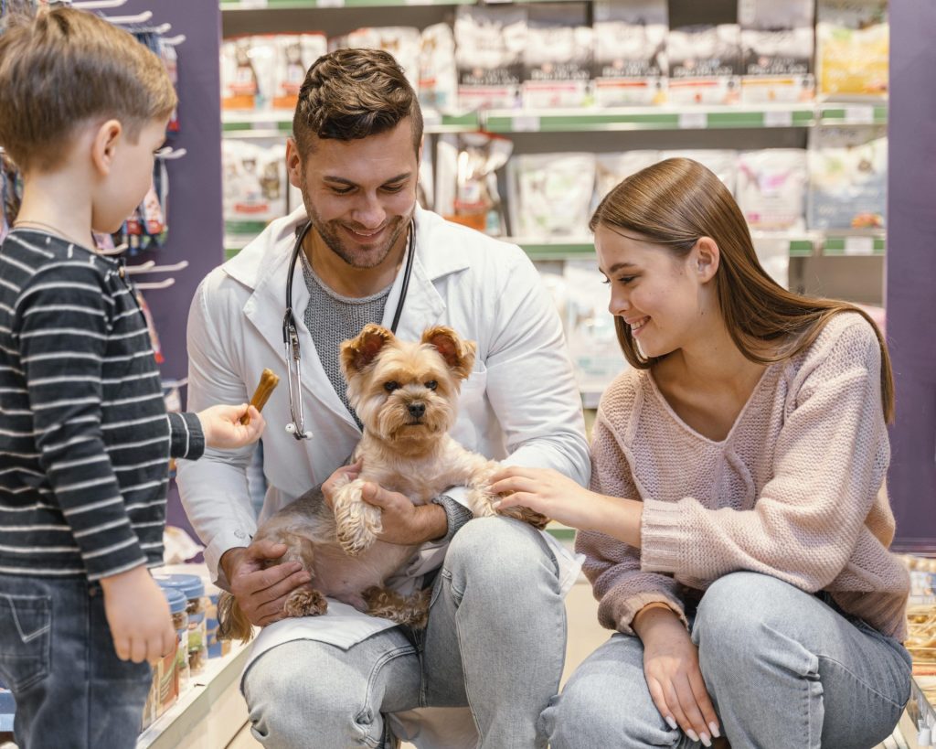 Un homme portant une blouse blanche interagit avec une famille et leur chien dans un magasin pour animaux.

