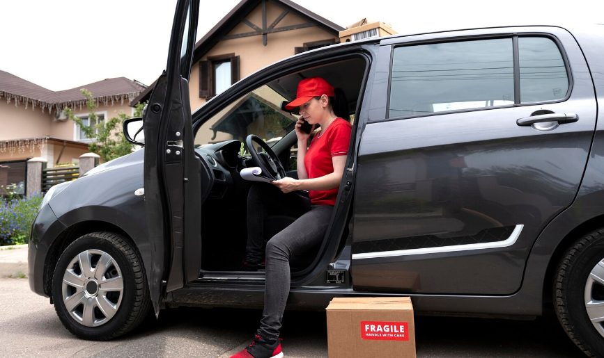 Livreuse en uniforme rouge gérant ses commandes depuis son véhicule utilitaire