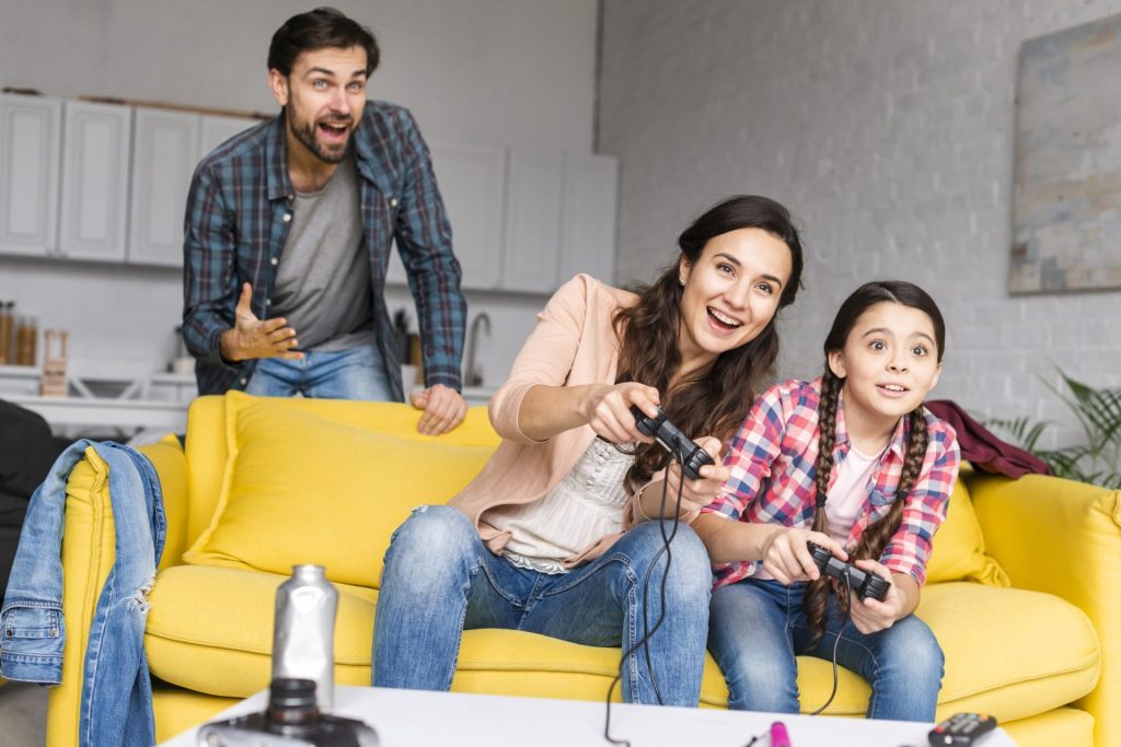 Famille qui joue ensemble aux jeux vidéo sur canapé, parents et enfant avec manettes