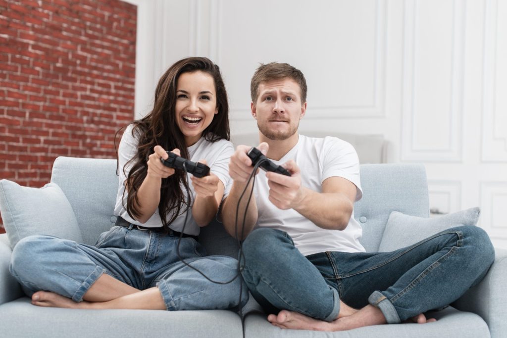 Couple qui joue aux jeux vidéo ensemble sur canapé avec des manettes de console