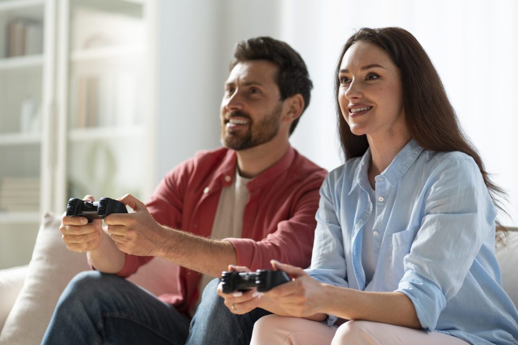 Couple jouant ensemble aux jeux vidéo dans un salon avec des manettes noires.