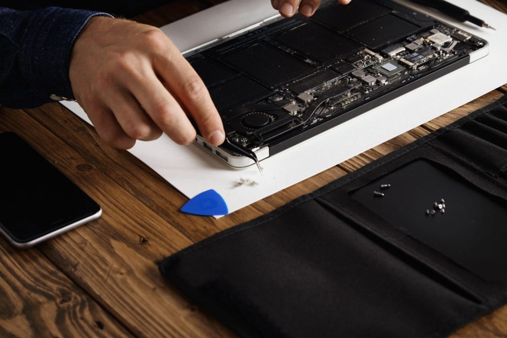 Technicien réparant l’intérieur d’un ordinateur portable ouvert sur une table en bois avec outils de maintenance informatique.