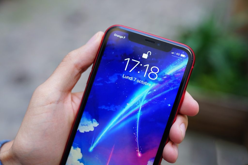 Smartphone rouge tenu en main affichant l'écran de verrouillage avec encoche Face ID visible