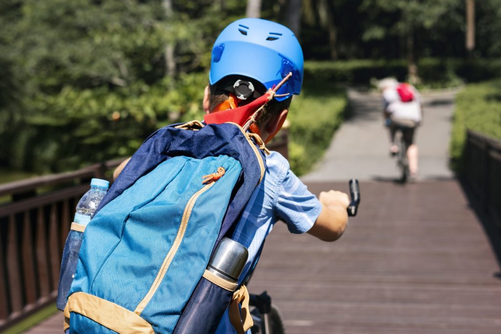 Casque de protection bleu porté par un jeune cycliste, sac à dos et gourde, sur une passerelle en bois