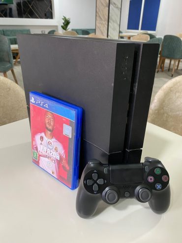 Console-PS4-Fat-noire-posee-sur-une-table-avec-sa-manette
