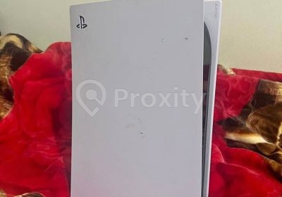 Vue arrière d’une console PlayStation 5 Standard blanche posée sur un lit à Douar Hicher