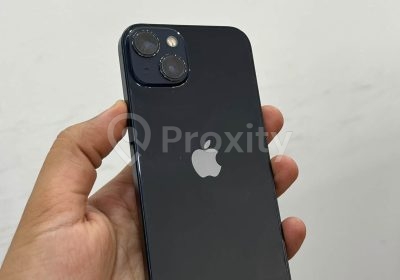Apple iPhone 13 noir 128 Go d'occasion photographié de dos dans une main, avec double appareil photo
